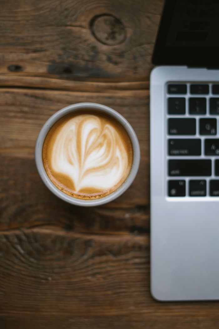 A latte with art next to a laptop on a wooden table, perfect for workspace themes.